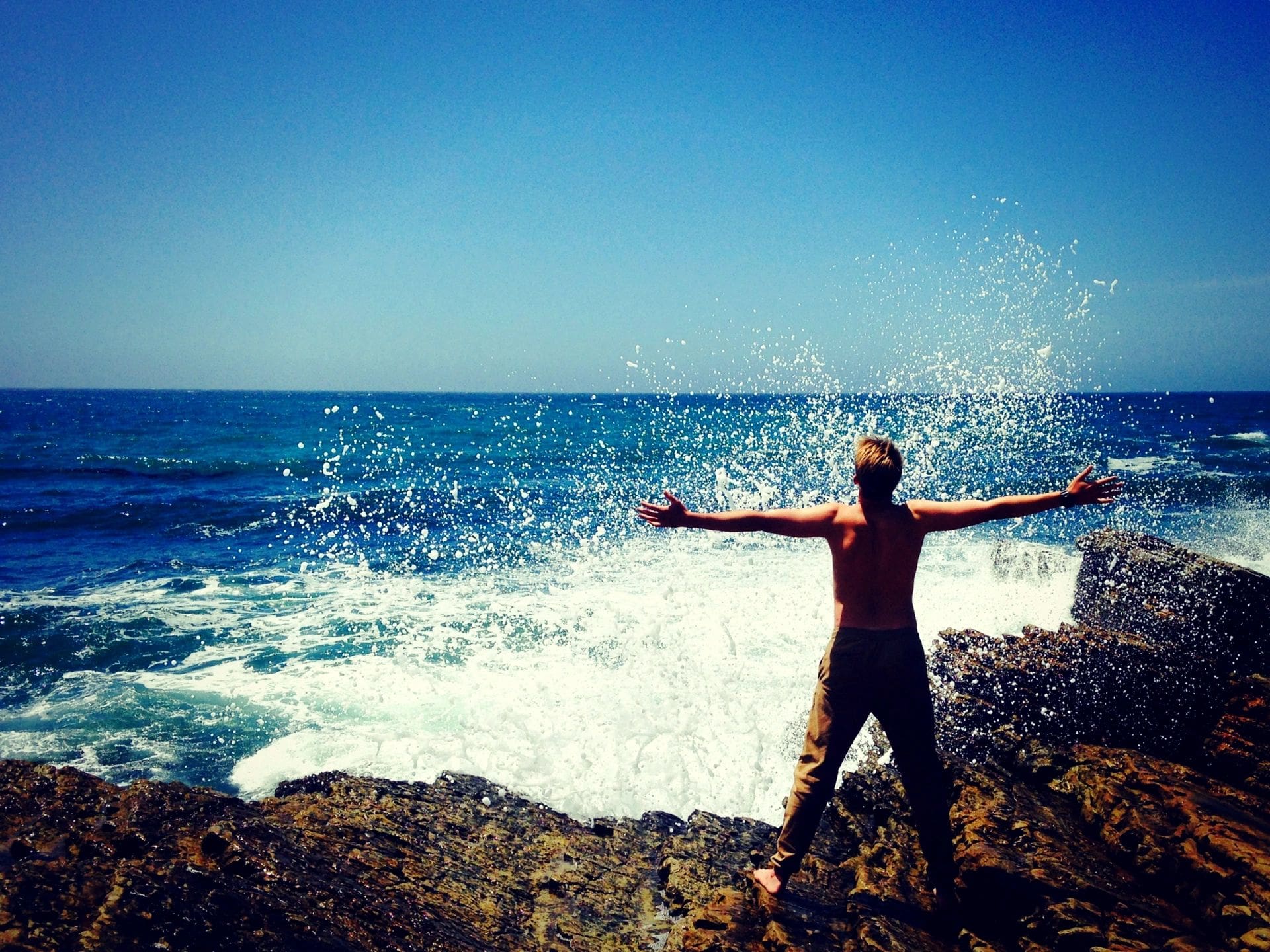 A person standing on top of a rock near the ocean.